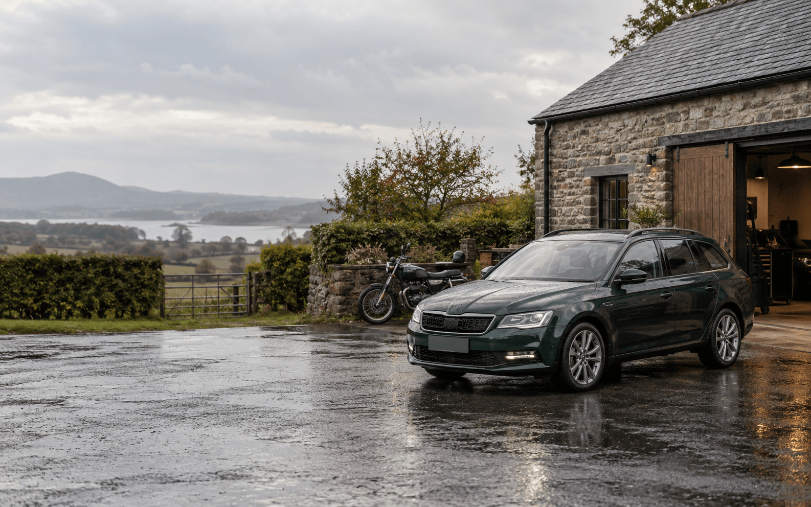 A dark green estate car and motorcycle outside a rural motor workshop